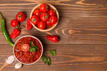 Composition with bowl of delicious salsa sauce and ingredients on brown wooden table