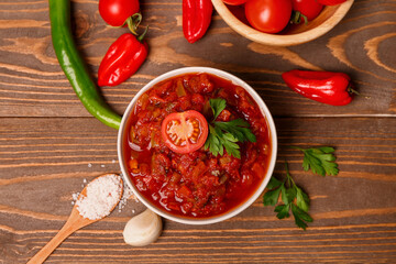 Bowl of delicious salsa sauce and ingredients on brown wooden table