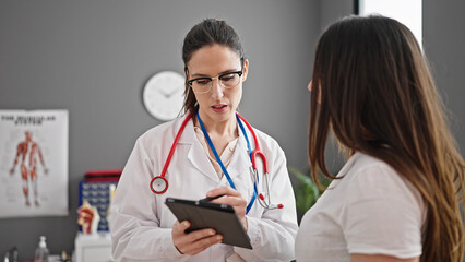 Fototapeta premium Two women doctor and patient using touchpad having consultation at clinic