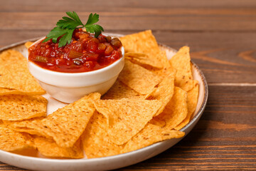 Plate with nachos and bowl of delicious salsa sauce on brown wooden table
