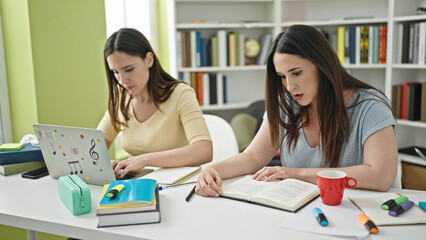 Two women sitting on table studying using laptop reading book at library university