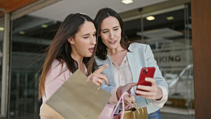 Two women going shopping holding bags using smartphone at street