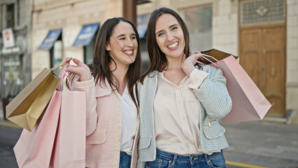 Two women smiling going shopping holding bags at street