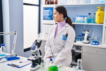 Young brunette woman working at scientist laboratory looking to side, relax profile pose with natural face with confident smile.