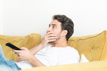 Fototapeta premium Shocked man sitting on the couch and watching tv at home 