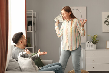Angry young woman with money shouting at her husband at home. Domestic violence concept