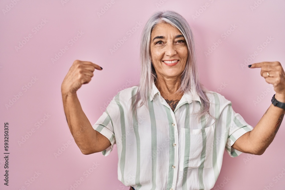 Sticker Middle age woman with grey hair standing over pink background looking confident with smile on face, pointing oneself with fingers proud and happy.