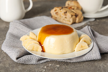 Plate with delicious pudding and bananas covered by caramel syrup on grey grunge background