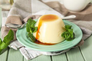 Plate with delicious pudding and mint covered by caramel syrup on green wooden table
