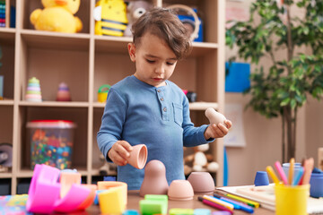 Adorable hispanic boy playing with toys standing at kindergarten