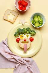 Plate with funny breakfast in shape of face and vegetables on beige background