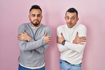 Homosexual couple standing over pink background shaking and freezing for winter cold with sad and...