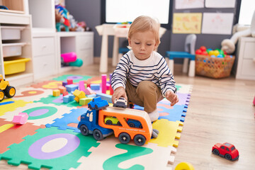 Adorable caucasian boy playing with car toy sitting on floor at kindergarten