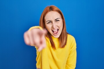 Fototapeta premium Young woman standing over blue background pointing displeased and frustrated to the camera, angry and furious with you