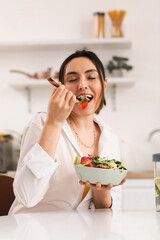 Young woman eating vegetable salad in kitchen