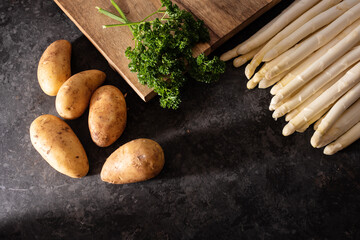 Fresh white asparagus and raw potatos with wooden cutting board Seasonal spring vegetables on...