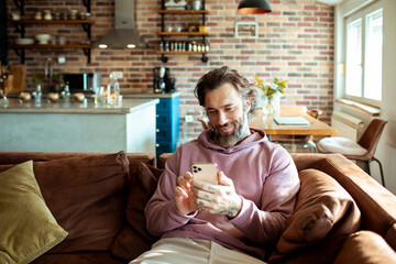 Young adult man using his phone while sitting on the couch in a living room