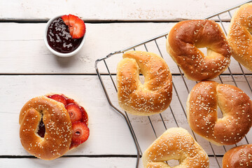 Grid of tasty bagels with sesame and strawberry jam on light wooden background, closeup