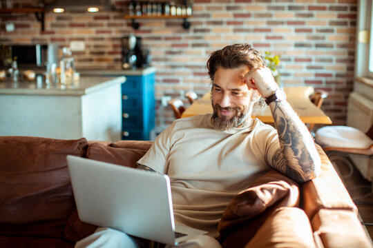Young adult man using a laptop on a couch in a living room
