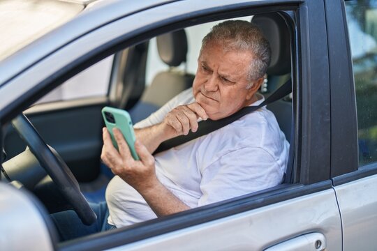 Middle age grey-haired man using smartphone sitting on car at street
