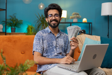 Planning budget. Rich happy indian man counting money cash use laptop computer calculate domestic...