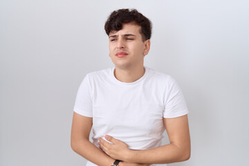 Young non binary man wearing casual white t shirt with hand on stomach because indigestion, painful illness feeling unwell. ache concept.