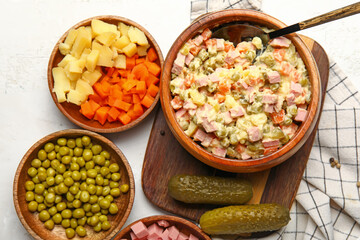 Bowl of tasty Olivier salad and ingredients on light background