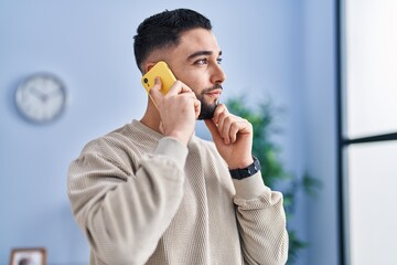 Young arab man talking on the smartphone with doubt expression at home