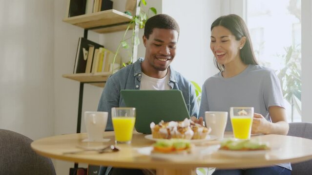 Multicultural couple having breakfast while using a laptop at home