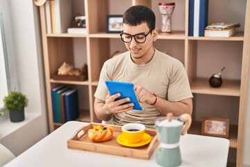 Fototapeta na wymiar Young man having breakfast using touchpad at home