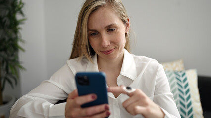 Fototapeta na wymiar Young blonde woman using smartphone sitting on sofa at home