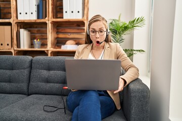 Young blonde woman working on online appointment scared and amazed with open mouth for surprise, disbelief face