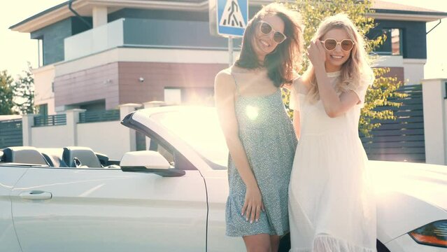 Two young beautiful and smiling hipster female in convertible car. Sexy carefree women posing near cabriolet. Positive models riding and having fun in sunglasses outdoors. Enjoying summer days
