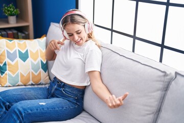 Obraz premium Young blonde woman listening to music doing guitar gesture at home