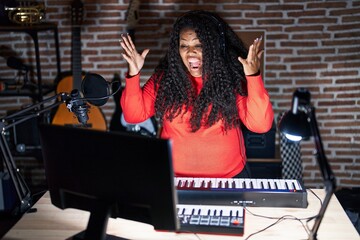 Plus size hispanic woman playing piano at music studio celebrating crazy and amazed for success with arms raised and open eyes screaming excited. winner concept