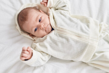 Adorable caucasian baby lying on bed with relaxed expression at bedroom
