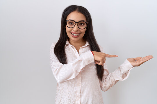Young arab woman wearing glasses over white background amazed and smiling to the camera while presenting with hand and pointing with finger.