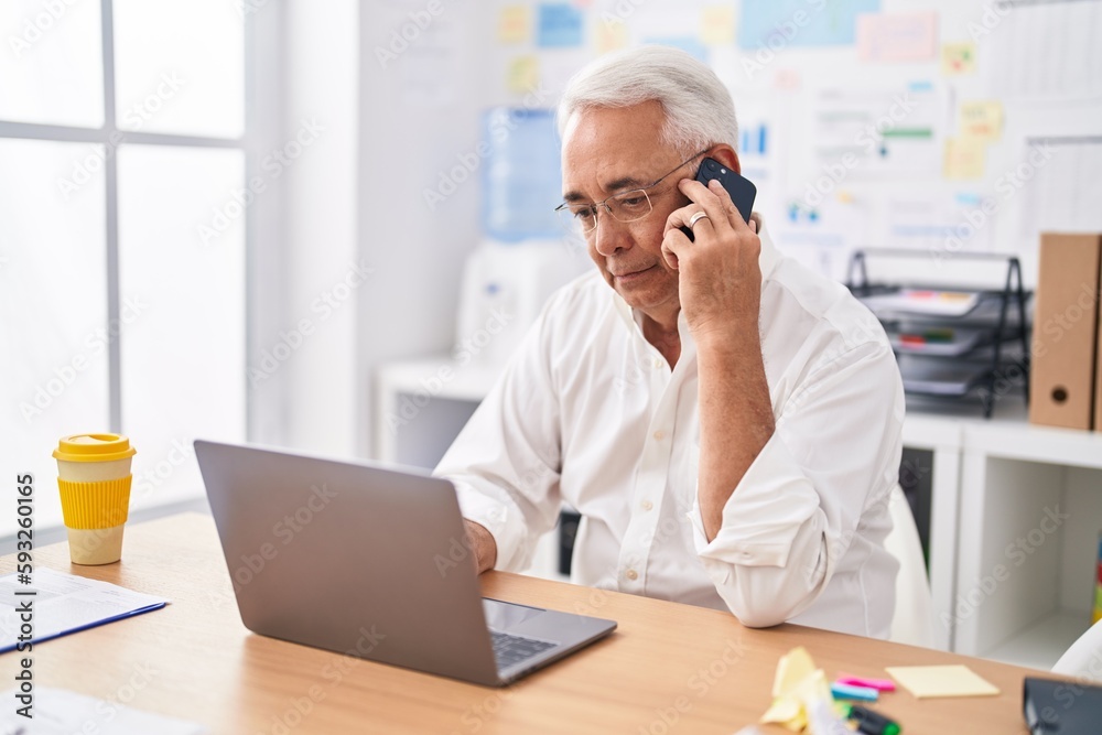 Wall mural Middle age grey-haired man business worker using laptop talking on smartphone at office