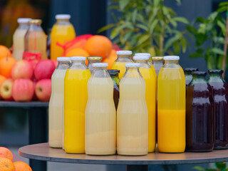 Close-up photo of organic fruit apple and orange juices in retro glass bottles placed on a table with fruit in blurred background