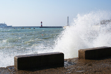 Sea waves breaking on the pier, resort embankment, sun glare on the water, background