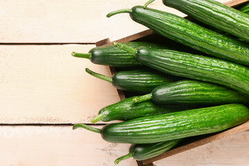 Box with fresh cucumbers on light wooden background, closeup