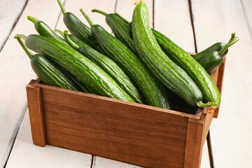 Box with fresh cucumbers on light wooden background