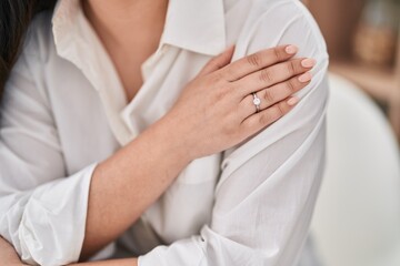 Young hispanic woman wearing engagement ring sitting on table at home