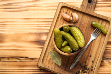 Bowl with tasty fermented cucumbers, board and ingredients on wooden background