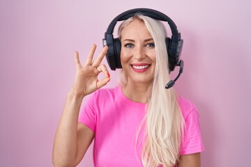 Caucasian woman listening to music using headphones smiling positive doing ok sign with hand and fingers. successful expression.