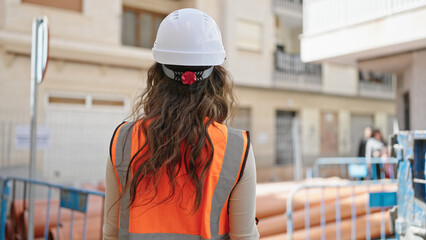 Young beautiful hispanic woman builder wearing hardhat backwards at street
