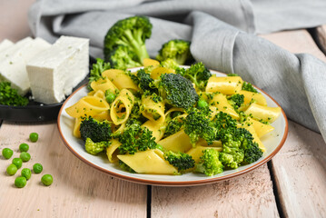 Plate with tasty penne pasta and broccoli on light wooden background