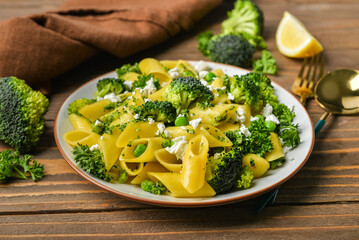 Plate with tasty penne pasta and broccoli on wooden background