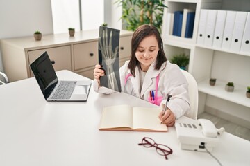 Down syndrome woman wearing doctor uniform holding x-ray at clinic