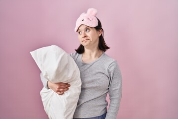 Woman with down syndrome wearing sleeping mask hugging pillow smiling looking to the side and staring away thinking.